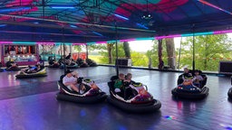 Verschiedene Menschen, vor allem Familien und Kinder, die Autoscooter fahren.