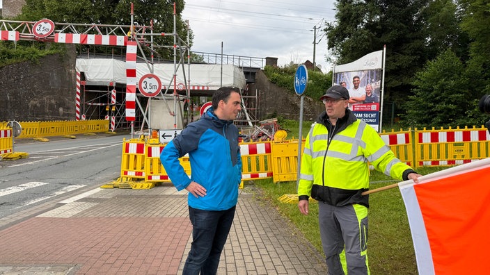 Bürgermeister Torben Blome spricht vor der Absperrung der Eisenbahnbrücke mit dem Warnposten Egon Hasse