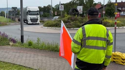 Brücken-Warnposten Egon Hasse hält mit einer Flagge den auf ihn zufahrenden LKW vor der Baustelle der Eisenbahnbrücke in Lügde an