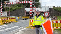 Egon Hasse steht mit einer Flagge vor der höhenbegrenzten Baustelle der Eisenbahnbrücke in Lügde