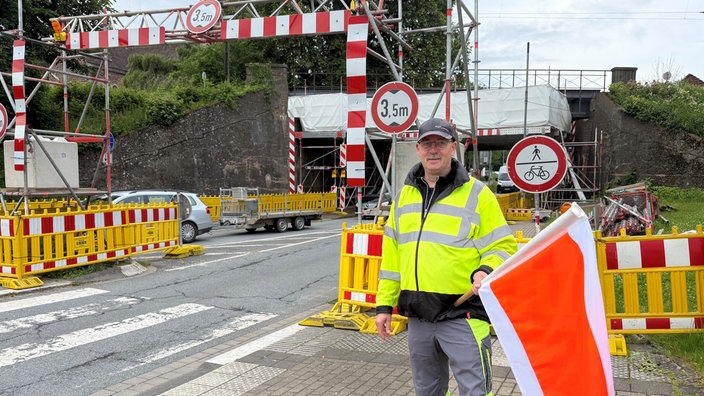 Egon Hasse steht mit einer Flagge vor der höhenbegrenzten Baustelle der Eisenbahnbrücke in Lügde