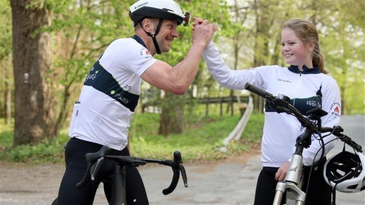 Oliver Wiehemeier und Anni Wein sitzen auf Fahrrädern und schlagen sportlich miteinander ein