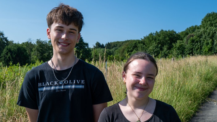Schüler und Schülerin lächeln in die Kamera.