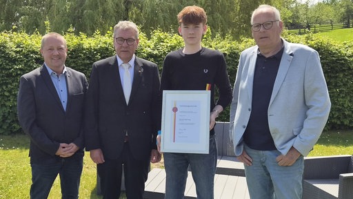 Jungschiedsrichter Jannes Hartwig hält eine Urkunde in den Händen, neben ihm stehen Landrat, Bürgermeister und Jannes' Großvater