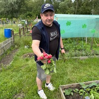 Ein Mann steht in einem Garten und hält einen frisch geerntetes Bund Radieschen in die Kamera.