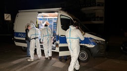 Mehrere Einsatzkräfte der Spurensicherung in Schutzanzügen stehen nachts an einem Polizeitransporter.