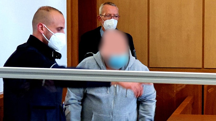 Vitalij K. läuft 2021 in den Gerichtssaal. Neben ihm steht ein Justizbeamter.