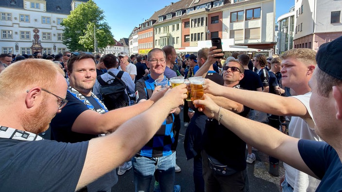 Mehrere Fans stehen im Kreis und stoßen mit ihrem Bier an.