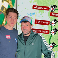 Links zwei lächelnde Männer, rechts eine marschierende Schützengruppe mit Trommeln und Uniformen. Im Hintergrund eine Landkarte mit grüner Route, Zielscheiben und roten Ortsschildern.