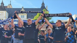 Fußballfans halten ihre Schals des SC Paderborn hoch und singen.