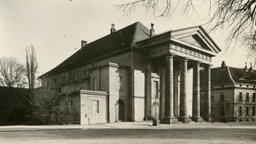 Auf dem Foto sieht man das Landestheater nach 1899. Es ist gebaut wie ein Haus. Vorne ein Vorbau mit drei Säulen.