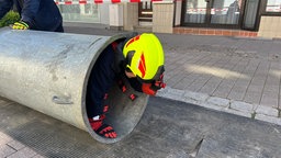 Eine Person in Feuerwehrkleidung kriecht durch ein großes Rohr