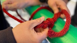 Hände knoten ein rotes Seil um eine grüne Stange