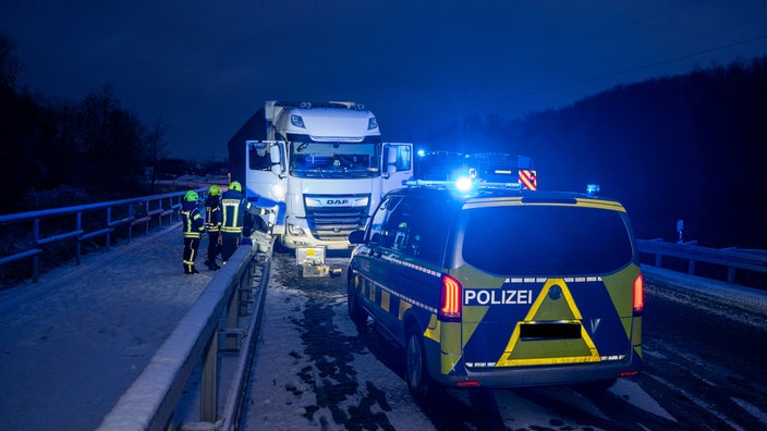 LKW-Unfall in Ahlen, Der weiße LKW ist in eine Leitplanke gefahren. Drum herum liegt Schnee. Einsatkräfte der Polizei stehen vor dem LKW. 