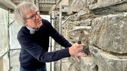 Norbert Sonntag steht neben der Kirchenwand. Er hält einen Hammer in der Hand 