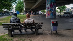 Kevin (will anonym bleiben) sitzt neben einer Person auf einer Bank. Wir sehen die Rückseite davon.