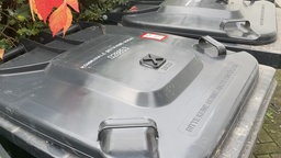 Auf einer Mülltonne klebt ein Sticker für sehbeeinträchtige Menschen. 