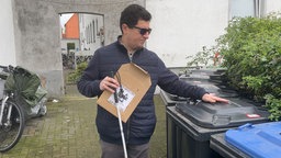 Ein sehbeeinträchtigter Mann ertastet einen Sticker auf einer Mülltonne. 