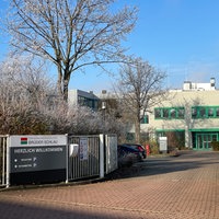 Ein graues Firmengebäude mit grünen Fenstern, die Bäume sind winterlich vereist, Firmenschild "Brüder Schlau - Herzlich willkommen"