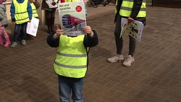 Ein Kind in Warnweste mit einem Plakat in der Hand.