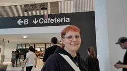 Eine junge Frau in der Universität, über ihr ist in Hintergrund ein Transparent zu sehen mit Aufschrift "Bildung ist kein Bonsai" 