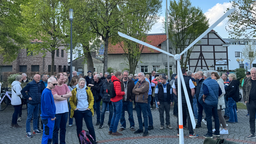 Demonstrierende vor einem kleinen Windrad, einer Art Nachbildung im Mini-Vormat