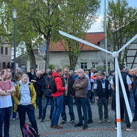 Demonstrierende vor einem kleinen Windrad, einer Art Nachbildung im Mini-Vormat