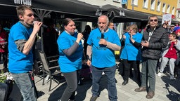 Mehrere Demo-Teilnehmer in blauen T-Shirts singen in Mikrofone