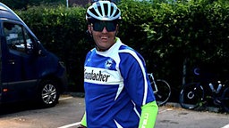 Ein Mann im Arminia-Bielefeld-Trikot und mit Radhelm auf dem Kopf lächelt