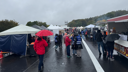 Zwischen Ständen stehen mehrere Menschen mit Regenjacken und Regenschirmen.