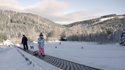 Zwei Personen fahren mit einem Skilift einen verschneiten Berg hoch