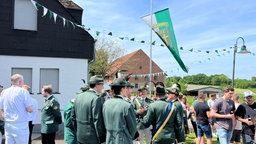 Schützen stehen auf dem Gelände eines Bauernhofs und unterhalten sich.