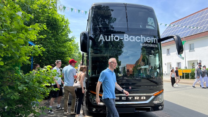 Mehrere Menschen stehen und gehen in der Umgebung eines Busses.