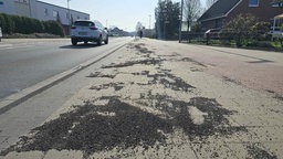 Massenweise kleine Steinchen liegen verstreut auf einem Bürgersteig und Radweg an einer Straße