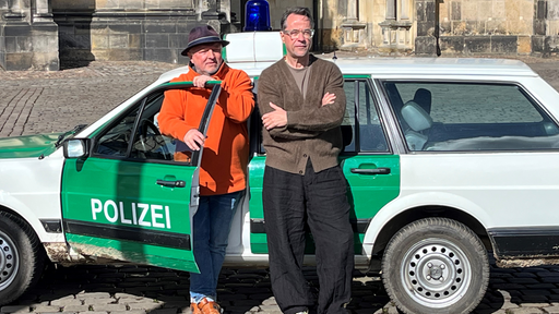Die Hauptdarsteller lehnen an dem Polizeitauto
