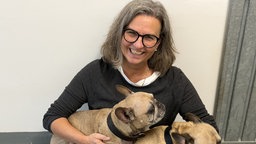 Sandra Kassenböhmer lacht in die Kamera mit zwei Hunden auf dem Schoß