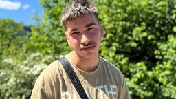 Ein junger Mann schaut mit einem ernsten Gesichtsausdruck in die Kamera. 