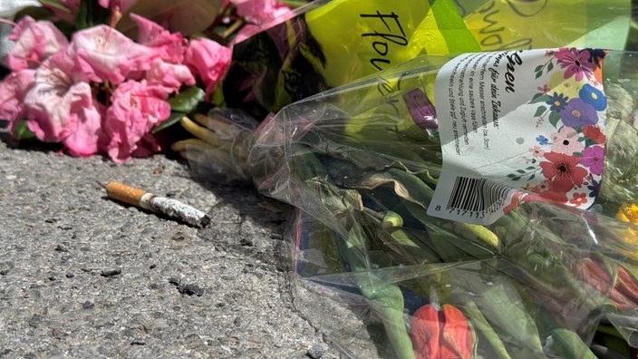 Auf dem Boden liegen Blumensträuße und eine Zigarette, die an den verstorbenen erinnern sollen. 
