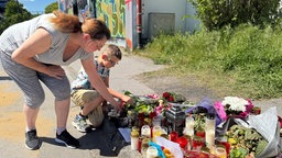 Eine Mutter und ihr Sohn knien vor der Gedenkstätte und legen Blumen nieder. 