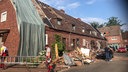 Vor einem stark beschädigten Wohnhaus tragen zwei Männer eine Leiter
