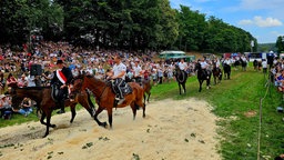 Die Teilnehmenden reiten auf Pferden hintereinander ein.