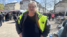 Eine Person in Arbeitskleidnung, im Hintergrund ist ein Trödelmarkt zu erkennen