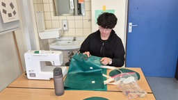 Ein Schüler näht eine Turnmatte zusammen