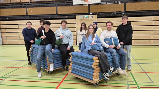 Die Schülergruppe und ihr Lehrer sitzen auf den Turnmatten