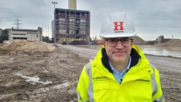 Ein Mann mit gelber Warnjacke und Helm steht auf einer Baustelle 
