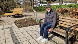 Ein Mann mit Brille sitzt auf einer Bank in einem Park.