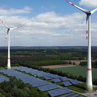 Zwei Windräder stehen auf einer freien Fläche, darunter Solaranlagen.