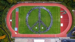 Drohnenaufnahme: Auf dem Sportplatz bilden die Schüler ein Peace-Zeichen
