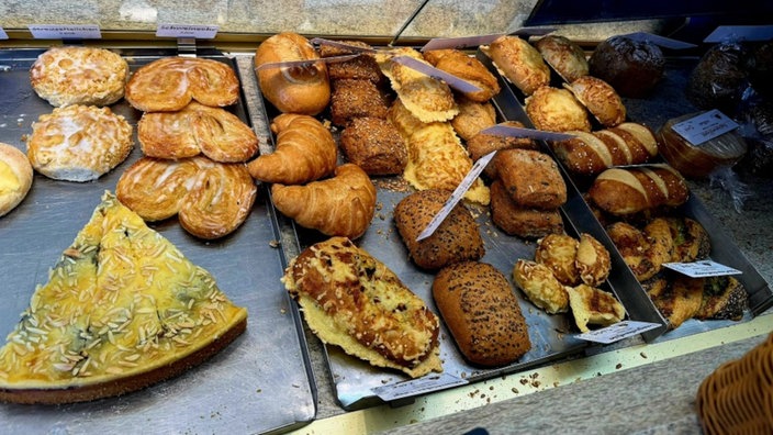 Ein paar Brötchen und Kuchen liegen in einer Auslage.
