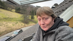 Frau Iris Gerstmann lehnt sich aus ihrem Dachfenster und schaut in die Kamera.